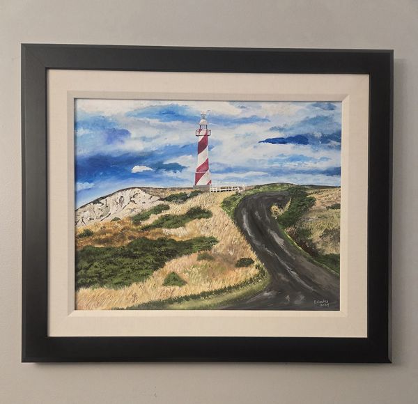 A Framed original acrylic painting of a Newfoundland lighthouse standing on a rugged rocky coastline beneath a brilliant blue sky overlooking the Atlantic Ocean